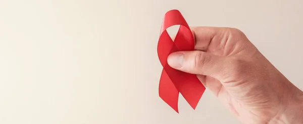 Mani che tengono il nastro rosso su sfondo rosso, consapevolezza hiv concep — Foto Stock