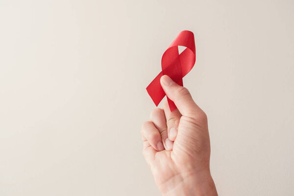 Hand holding red ribbon on red background, hiv awareness concept