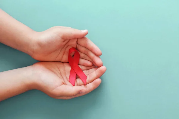 Mavi arka planda kırmızı kurdele tutan eller, HIV farkındalığı gizliyor — Stok fotoğraf