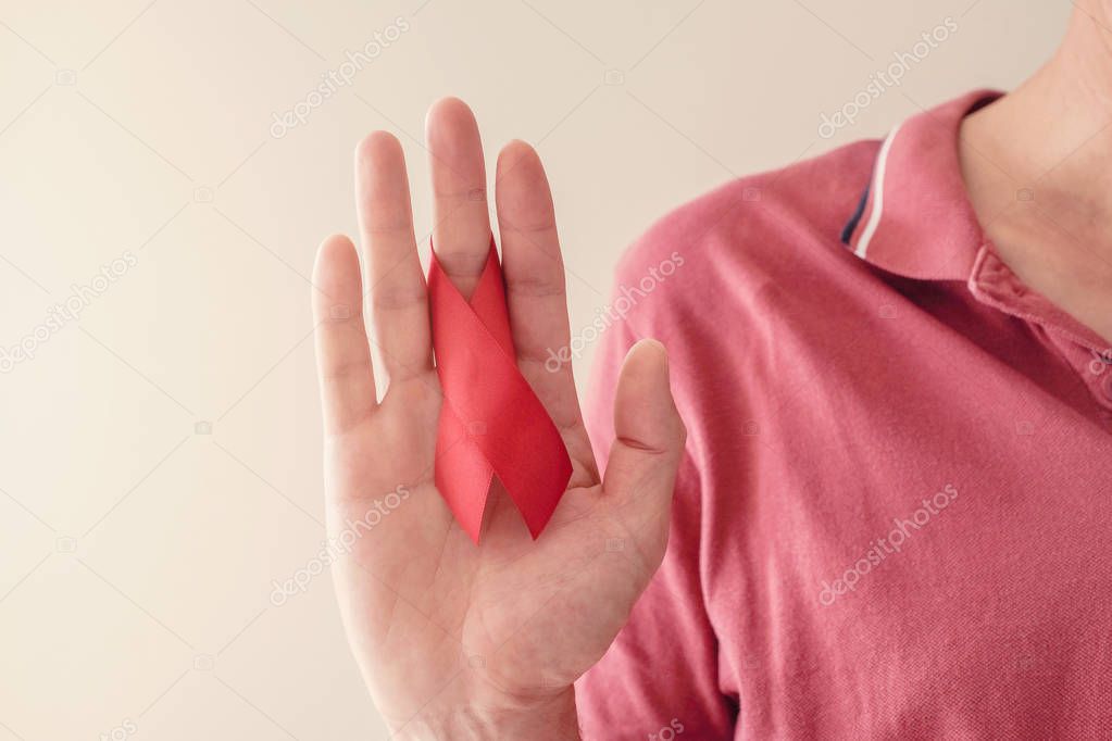 Hands holding red ribbon on red background, hiv awareness concep