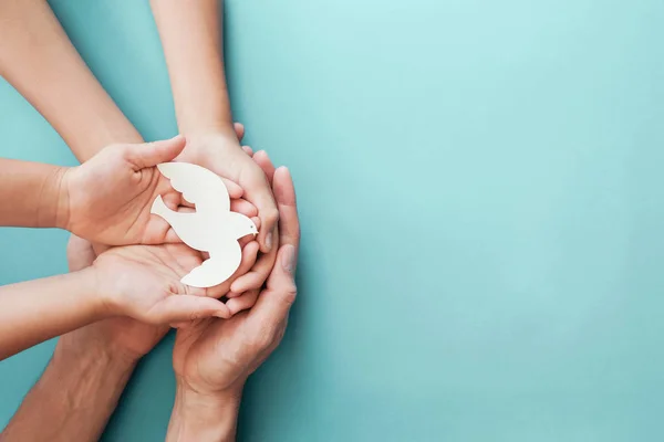 Yetişkin ve çocuk elleri mavi arka planda beyaz güvercin kuşu tutuyor