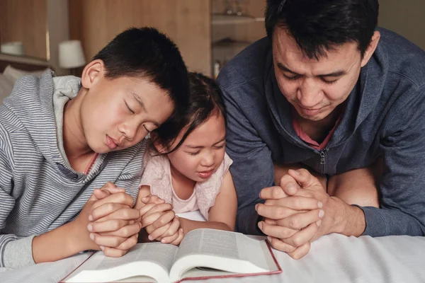 Діти і батько батько моляться з Біблією на ліжку, сім'я — стокове фото