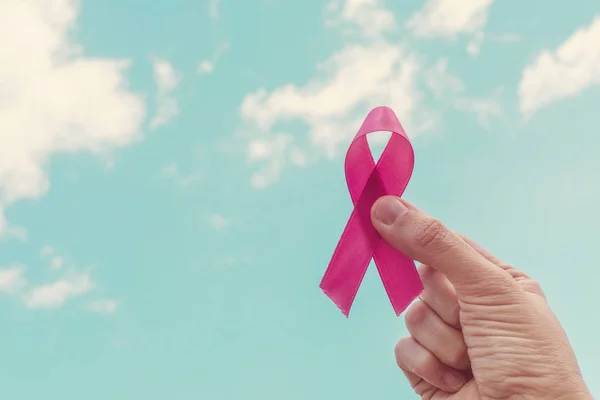 Mão segurando fita rosa sobre o céu azul, dia mundial do câncer, mama — Fotografia de Stock