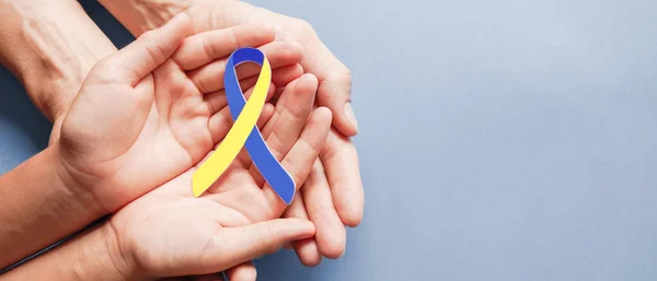 青と黄色のリボン状の紙を保持大人と子供の手 ダウン症候群の意識 世界ダウン症候群の日 — ストック写真