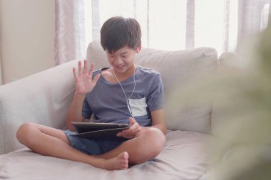 Genç Asyalı çocuk evde dijital tablet kullanıyor, podcast, oyun, çevrimiçi eğitim, uzaktan öğrenme, evde eğitim, sosyal uzaklık, izolasyon, facetime veya zoom uygulaması kavramını kullanıyor