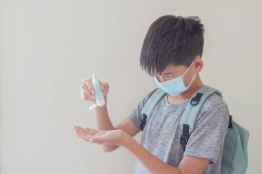 Maske takan ve el dezenfektanı kullanan Asyalı çocuk, okul yeniden açılıyor, covid-19 koronavirüs salgını bittikten sonra okula dönüyor, yeni normal konsept.