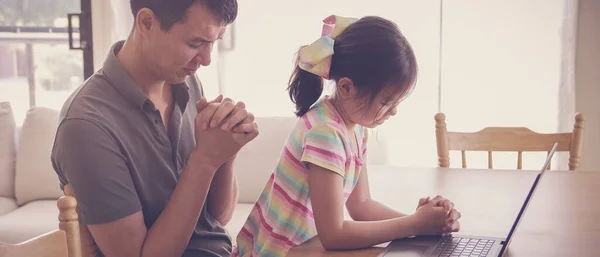 Young girl praying with father parent with laptop, family and kids worship online together at home, streaming church service, social distancing concept