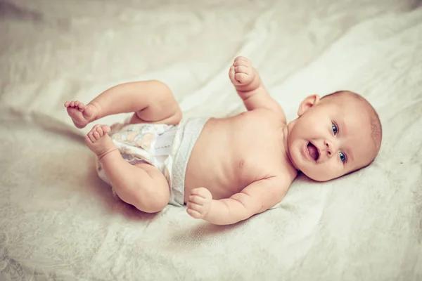 Happy baby lying on white sheet and holding his legs — Stock Photo, Image