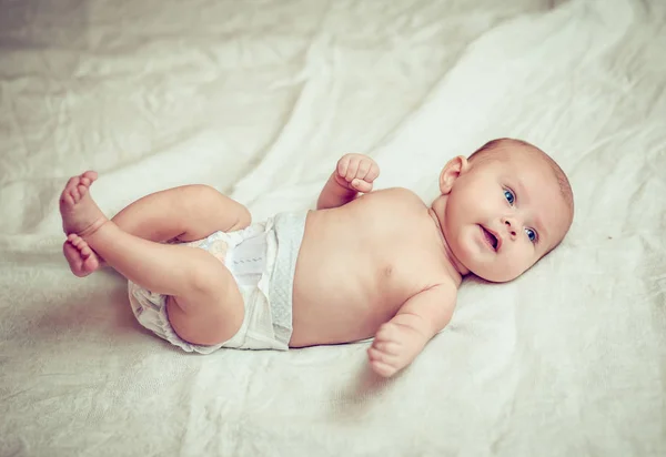 Feliz bebé acostado en sábana blanca y sosteniendo sus piernas — Foto de Stock