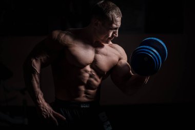 Siyah arka plan üzerinde halter alıştırmalar yapan kaslı vücut geliştirmeci adam