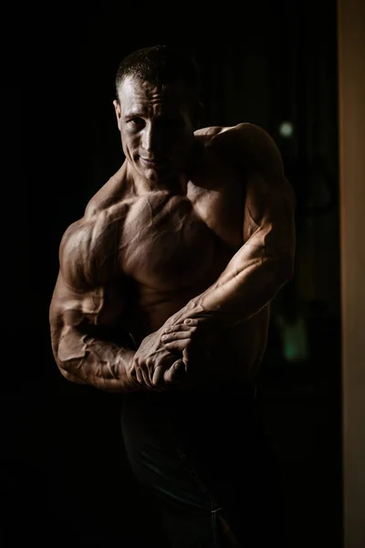 Muscular bodybuilder guy doing exercises with dumbbell over black background — Stock Photo, Image