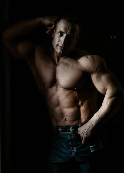 Muscular bodybuilder guy doing exercises with dumbbell over black background — Stock Photo, Image