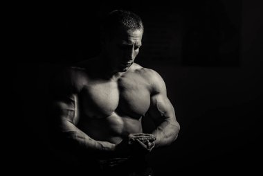 Siyah arka plan üzerinde halter alıştırmalar yapan kaslı vücut geliştirmeci adam