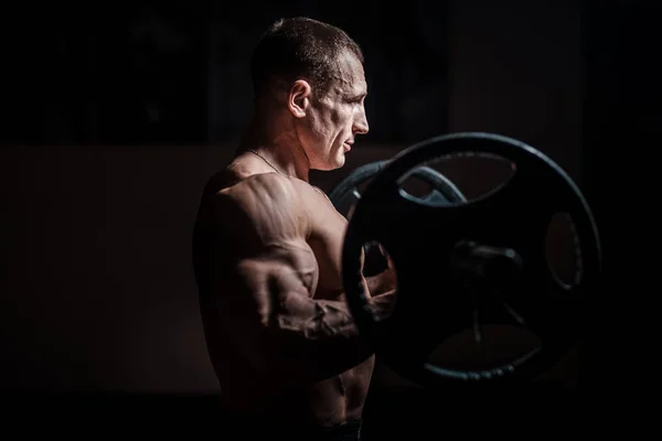 Musclé bodybuilder gars faire des exercices avec haltère sur fond noir — Photo