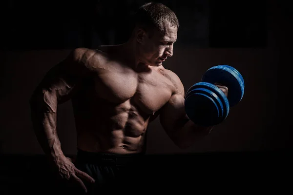 En muskuløs kroppsbygger som gjør øvelser med ringeklokke over svart bakgrunn – stockfoto