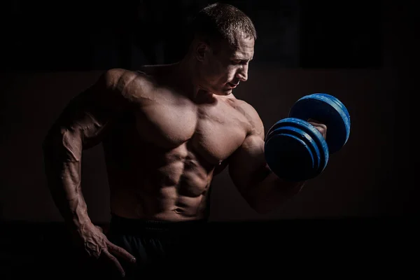 Muscular bodybuilder guy doing exercises with dumbbell over black background — Stock Photo, Image