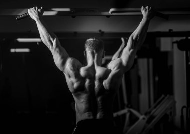 Siyah arka plan üzerinde halter alıştırmalar yapan kaslı vücut geliştirmeci adam