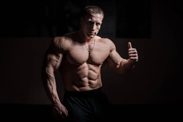 Muscular bodybuilder guy doing exercises with dumbbell over black background — Stock Photo, Image