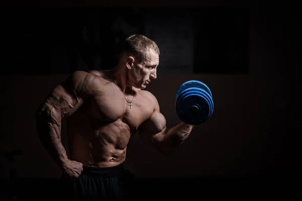 Muscular bodybuilder guy doing exercises with dumbbell over black background — Stock Photo, Image