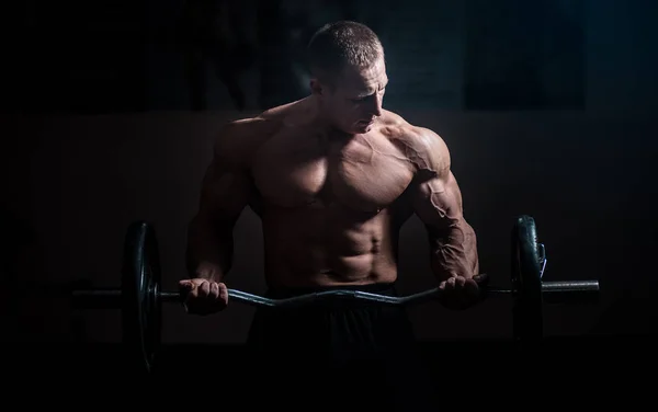 Siyah arka plan üzerinde halter alıştırmalar yapan kaslı vücut geliştirmeci adam