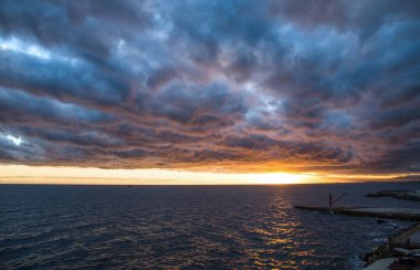 Gün batımında bulutlu bir gökyüzünün altındaki iskelede kırmızı vinç..