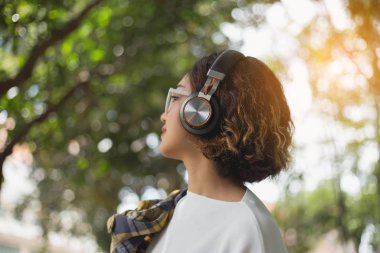 Genç bir kız çimlere uzanıp müzik dinliyor, yumuşak ve bulanık arka planda rahatlıyor.