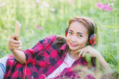 Genç bir kız çimlere uzanıp müzik dinliyor, yumuşak ve bulanık arka planda rahatlıyor.