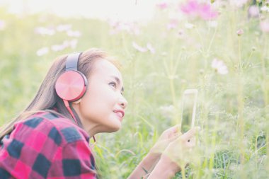 Genç bir kız çimlere uzanıp müzik dinliyor, yumuşak ve bulanık arka planda rahatlıyor.