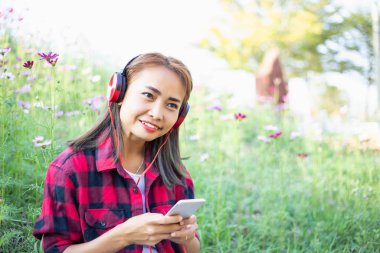 Genç bir kız çimlere uzanıp müzik dinliyor, yumuşak ve bulanık arka planda rahatlıyor.