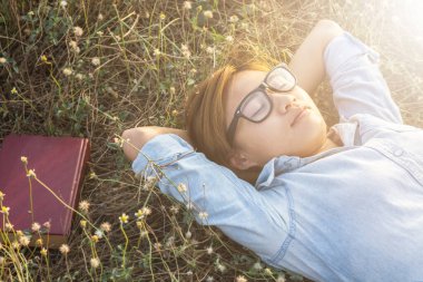 Genç bir kız çimlere uzanıp müzik dinliyor, yumuşak ve bulanık arka planda rahatlıyor.