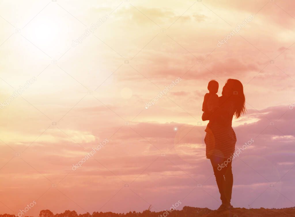 Mother holding baby walking on the sunset background