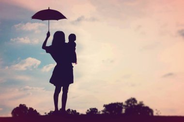 Anne kucağında bebekle gün batımında yürüyor..