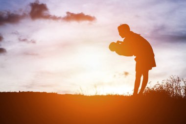 Anne kucağında bebekle gün batımında yürüyor..