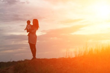 Anne kucağında bebekle gün batımında yürüyor..