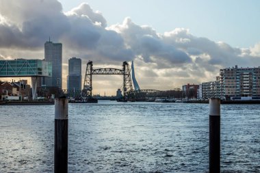 Rotterdam 'da kışın şehir manzarası, gökyüzünde güzel bulutlar ve güneş, modern gökdelenler ve güzel binalar ve Yeni Maas' ın üzerindeki Erasmus ve Willemsbridge.