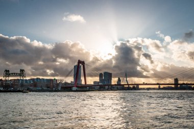 Rotterdam 'da kışın şehir manzarası, gökyüzünde güzel bulutlar ve güneş, modern gökdelenler ve güzel binalar ve Yeni Maas' ın üzerindeki Erasmus ve Willemsbridge.