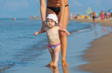 Anne kızı sahile yürümeyi öğretiyor.