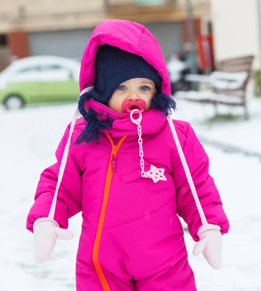Tipegő baba lány játszani a hóban bíbor hó öltönyt. — Stock Fotó