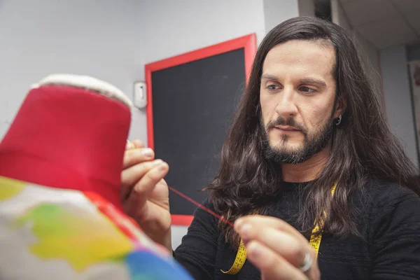 Long-haired young man holding a red thread in front of a mannequin