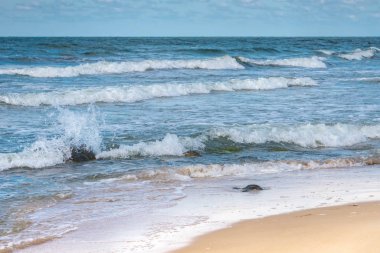 Kum kıyısındaki deniz suyundaki taşlar. Fırtınada Baltık Denizi