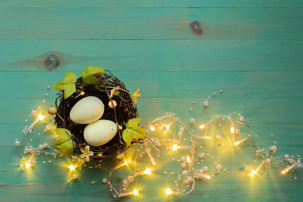 Œufs de Pâques dans le nid et lumières guirlande autour sur fond de bois peint vert rustique — Photo