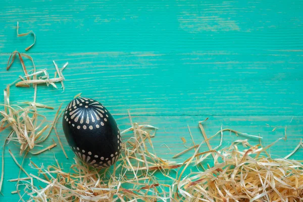 Osterhintergrund mit einem schwarz bemalten, gemusterten Osterei und Strohhalmen — Stockfoto