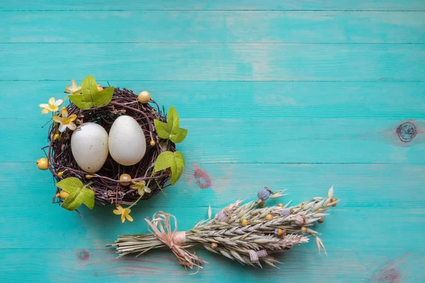 Œufs de Pâques dans le nid et le bouquet de blé sec et de fleurs sur fond de bois vintage — Photo