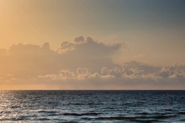 Gün batımında denizin parlak ve koyu mavi yüzeyi ve kümülüs bulutuyla gökyüzü.