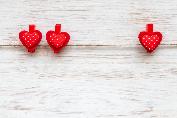 Twee en een rode polka-dot hartjes op wasknijpers aan houten rand. Valentijnsdag achtergrond met harten — Stockfoto