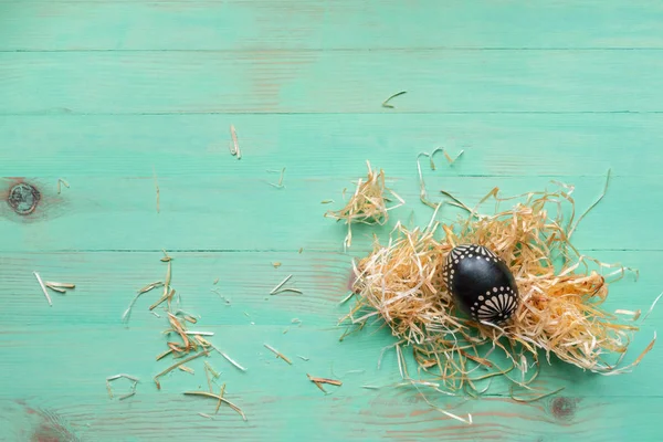 Oeuf de Pâques en bois peint en noir et pailles de foin sur fond de bois — Photo