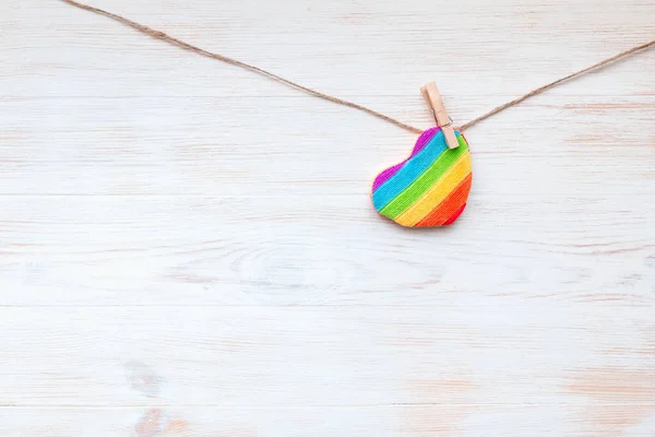 One rainbow heart-shaped pillow on clothespin on wooden border. Valentines day concept. Background for LGBT.