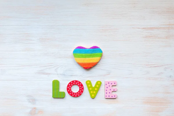 LOVE word in wood letters and rainbow heart shape pillow on wood vintage board. Valentines day concept. Mockup for LGBT.