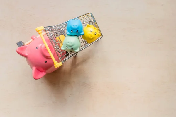 Big pig bank holding shopping cart with little pigs banks on wood background. One big pig bank rolling three piglet banks in trolley cart. Pig banks in shopping cart. Top view. Saving money concept