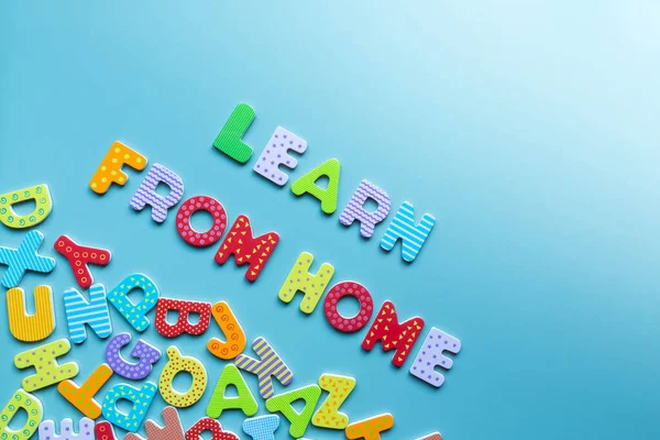 Words LEARN FROM HOME of colorful wooden letters and scattered letters on blue background. Inscription learn from home on board with copy space. Home education concept. Homeschooling